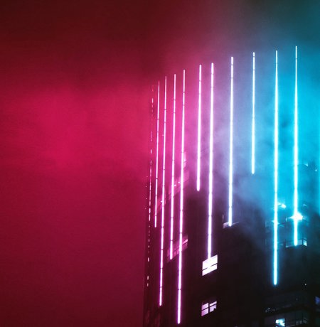 Modern high rise building with blue neon lights vertically along the building front