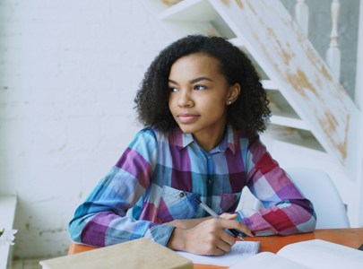 Young girl with pen in her hand staring out the window while studying